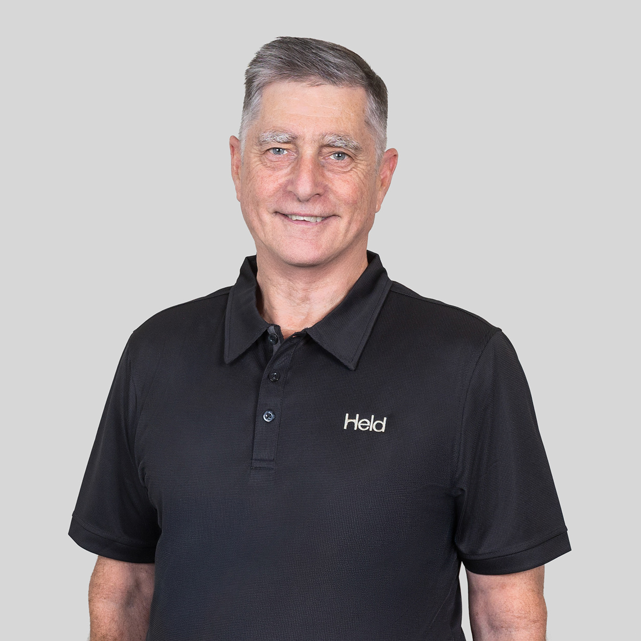 Portrait of a smiling man wearing a black polo shirt with the Held logo on the chest.